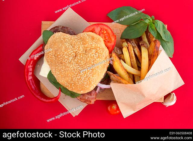 Heart shaped hamburger, love burger fast food concept, Valentines day surprise dinner, red background, top view flat lay