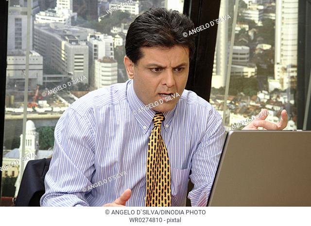 Executive looking at screen of laptop with worried angry expression in office at top floors of skyscraper in modern city MR 687U