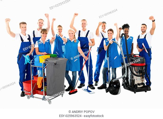 Portrait of happy multiethnic janitors with arms raised holding cleaning equipment against white background