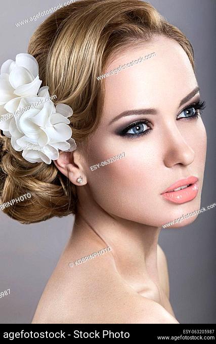 Portrait of a beautiful blonde woman in the image of the bride with flowers in her hair. Picture taken in the studio on a blue background