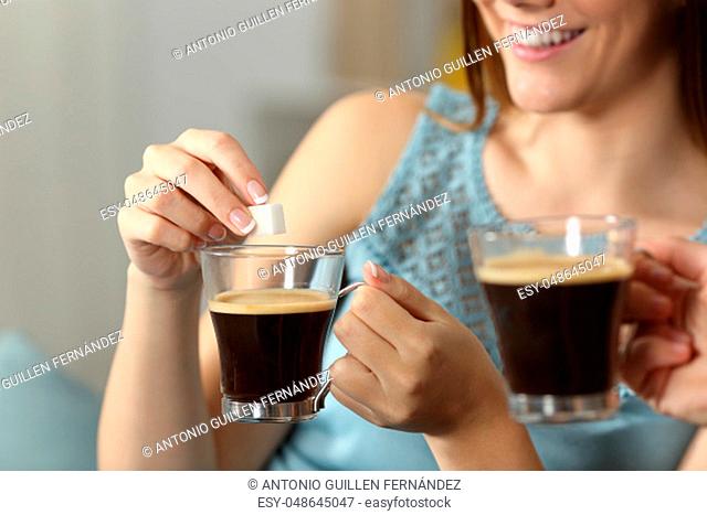 Close up of a women hands throwing sugar into a coffee cup sitting on a couch in the living room at home
