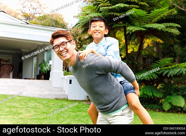 Portrait of happy asian father carrying his son and smiling outdoors in garden