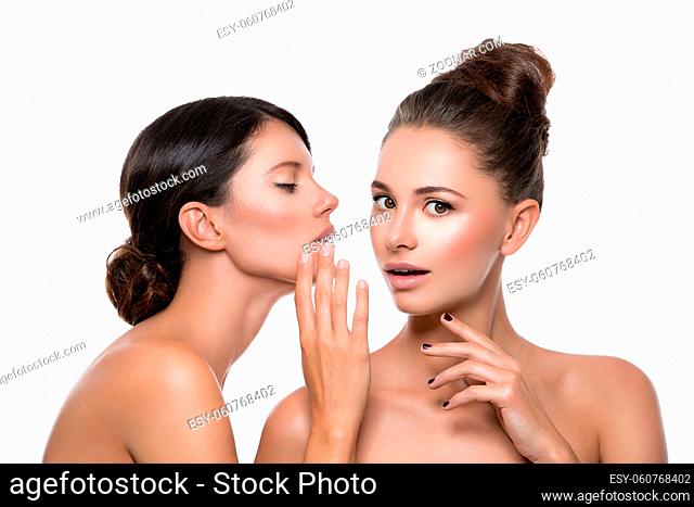 Two beautiful young women with perfect skin gossiping about somthing. Isolated over white background. Beauty shot. Copy space