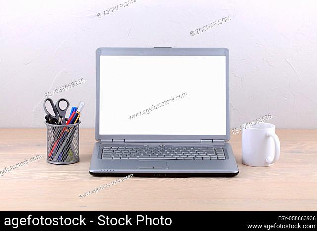 A laptop computer on office desk coffee mug and pens. White screen template with clipping path