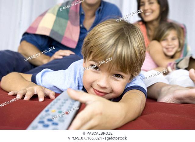 Portrait of a boy holding a remote control with his parents and his sister behind him