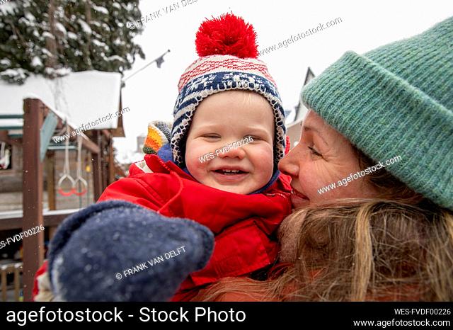 Smiling woman looking at cheerful son while standing at backyard during winter
