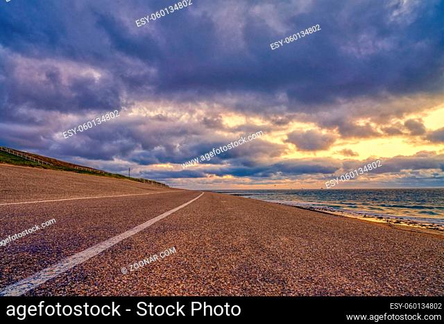 Landscape, seascape sunset on the coast of Huisduinen. The detailed road with white stripe leads to infinity. Colorful landscape and seascape with street