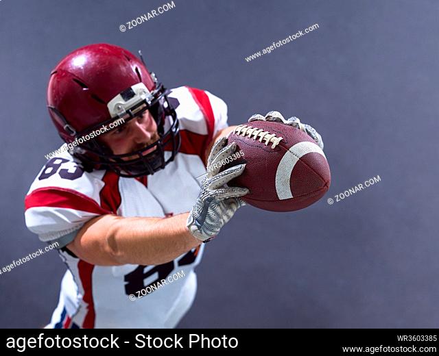 Portrait of american football player showing football to camera against gray background