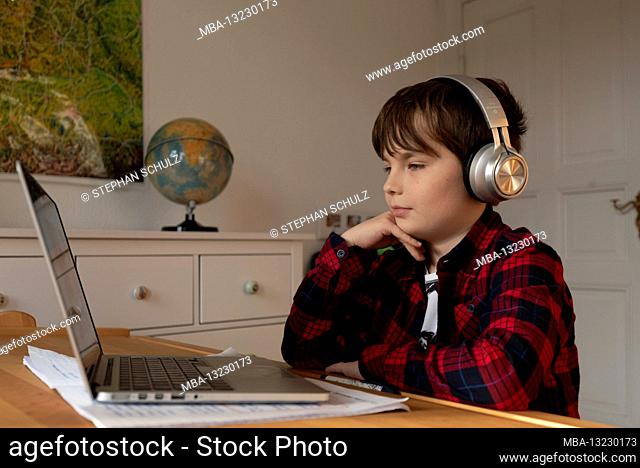 A boy sits at his desk in homeschooling while a teacher video calls questions about distance learning