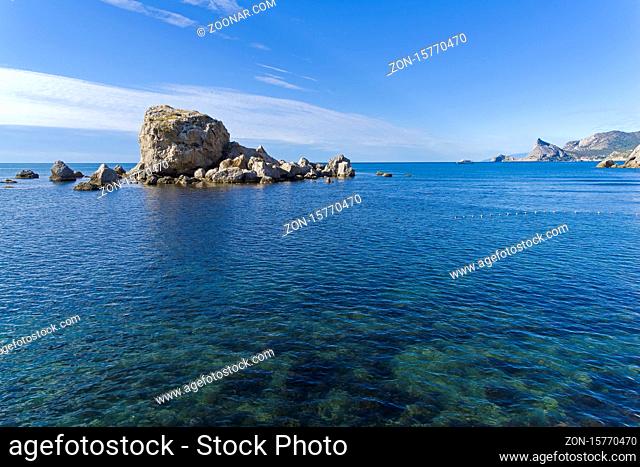 A small rocky island near the sea shore. View from the quay of the resort town of Sudak, Crimea. Sunny day in September