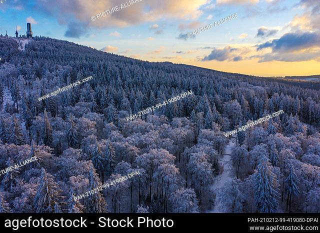 12 February 2021, Hessen, Sandplacken: The sun sets behind the trees covered with snow and ice at the Feldberg in Taunus (aerial view with a drone)