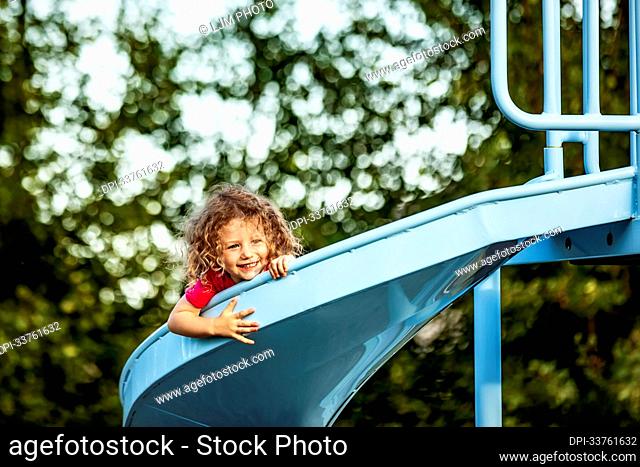 Young girl sliding down on a slide in a playground; St. Albert, Alberta, Canada