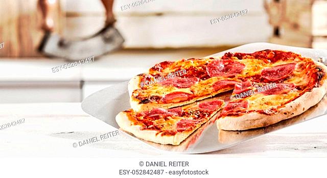 Freshly prepared Italian salami pizza served on a metal paddle in a pizzeria with a wedge portion cut out as a tasty snack or lunch