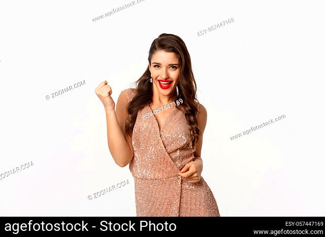 Celebration and party concept. Elegant young woman winning and feeling satisfied, wearing glamour dress, making fist pump and say yes