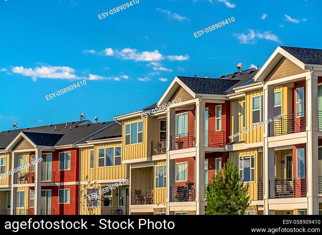 Lovely townhomes viewed against blue sky background on a sunny day. The multi-storey residences with balconies have red and cream exterior walls