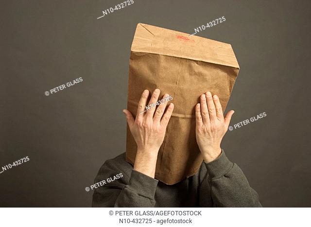 Man whose head is covered with a paper bag and whose hands are touching it