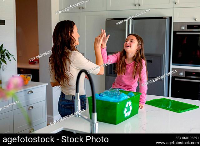 Happy caucasian mother and daughter segregating rubbish and giving high five