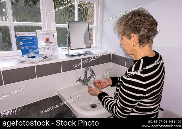 England, UK. 2021. An elderly woman washing her hands before taking a home coronavirus test from items on the windowsill