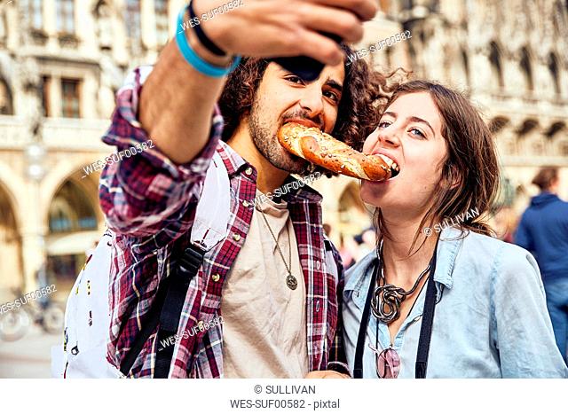 Young couple taking a selfie with brezel in the mouth, Munich, Germany