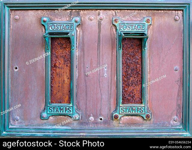 old british postal mail boxes with rusted letter slots and ornate green copper frames with the words postage stamps surrounded by an old stained metal frame