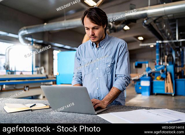 Young businessman using laptop while standing at factory