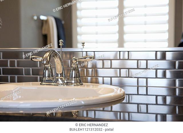 Faucet and spigots at sink with metallic backsplash in bathroom; Murrieta; California; USA