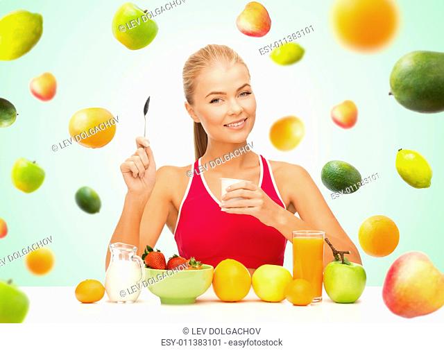healthy eating, diet, organic food and people concept - happy woman eating yogurt and having breakfast over green background with falling fruits