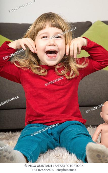 funny portrait of three years old child, with red and green clothes, looking, laughing and teasing with hands in ears and open mouth