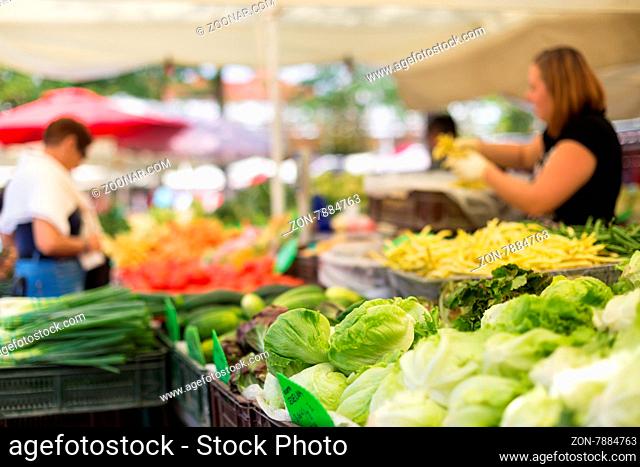 Farmers#39; food market stall with variety of organic vegetable. Vendor serving and chating with customers