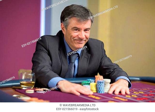 Man smiling and taking his chips on roulette table