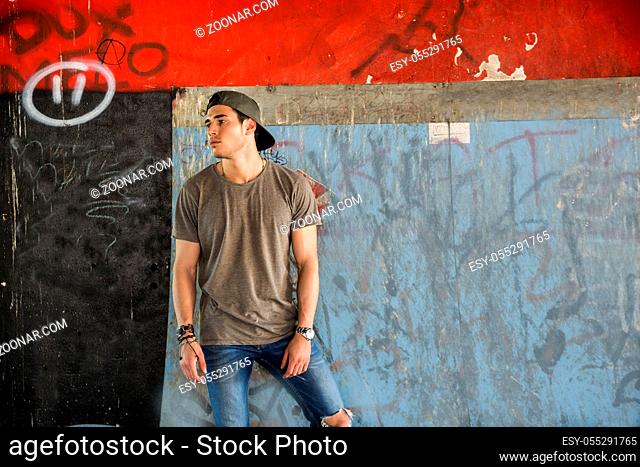 Attractive young man standing against colorful wall, looking away