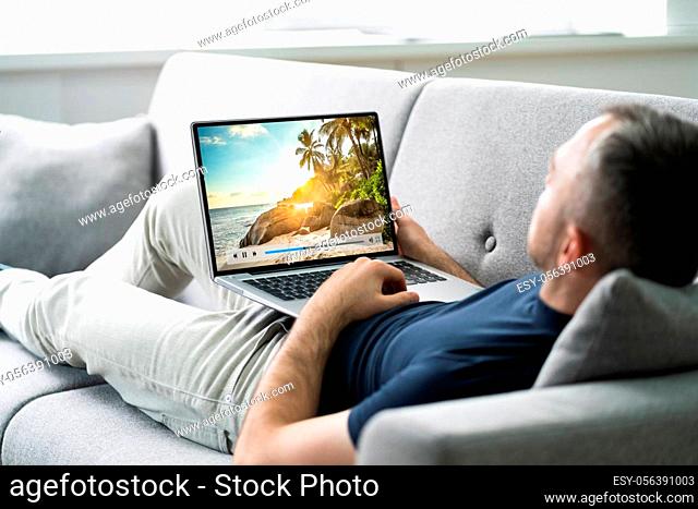 Young Man Lying On Sofa Watching Video On Tablet