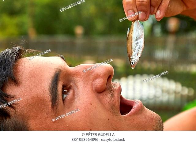 Man holding a tiny fish pretending to eat it
