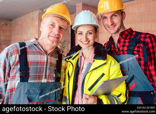 Young smiling female engineer holding digital tablet in hand posing with two male at construction site