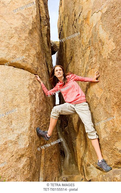 USA, California, Joshua Tree National Park, Young woman climbing canyon walls