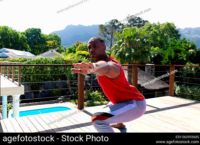 Active african american man practicing yoga at terrace on sunny day