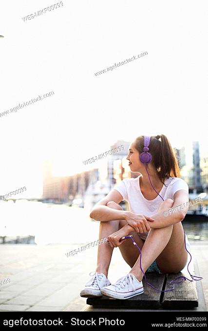 Young woman with headphones sitting on bench at promenade
