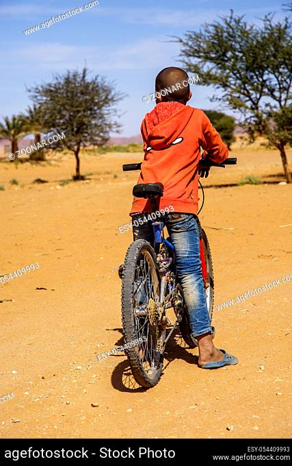 Tinzouline, Morocco - February 26, 2016: Rear view of Moroccan boy riding bicycle in desert in Tinzouline village in Morocco