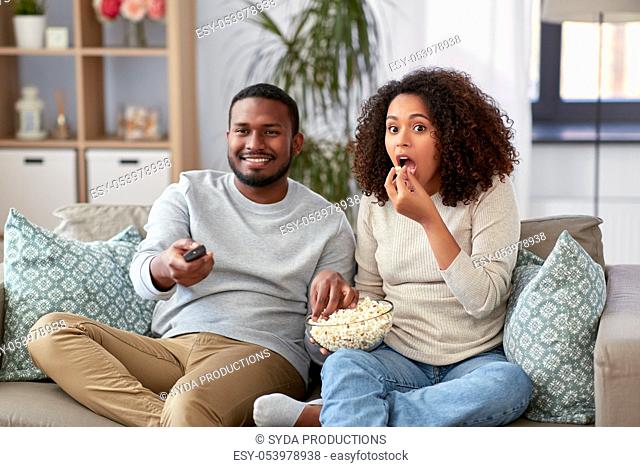 african couple with popcorn watching tv at home