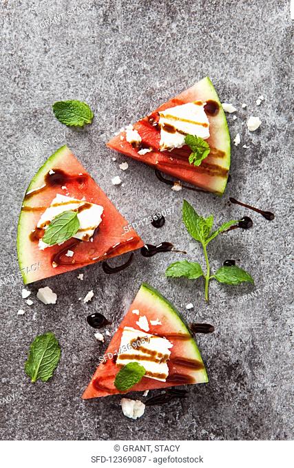 Three slices of fresh watermelon topped with feta cheese, balsamic syrup and fresh mint leaves