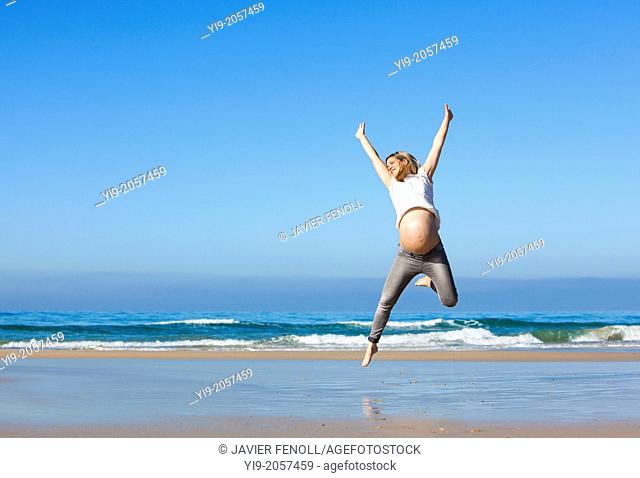 pregnant woman jumping on the beach