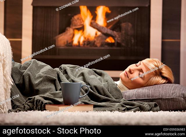 Woman sleeping at home lying on floor in front of a fire place