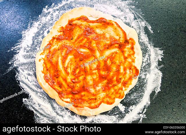 Preparing pizza, close-up of pizza dough with tomato sauce