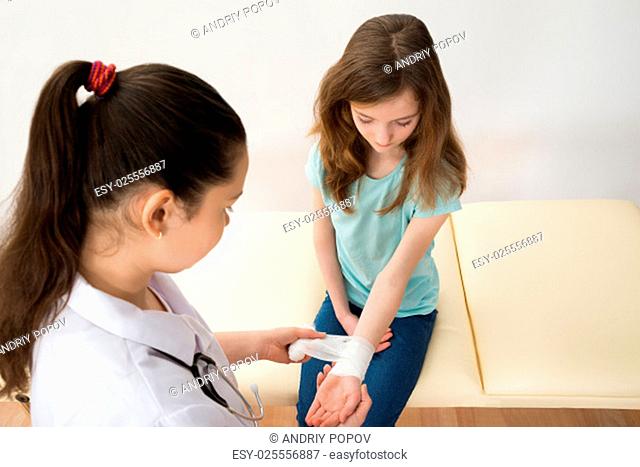 Female Doctor Bandaging Hands Of Girl Child In Clinic