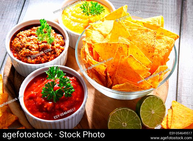 Composition with glass bowl of tortilla chips and dipping sauces