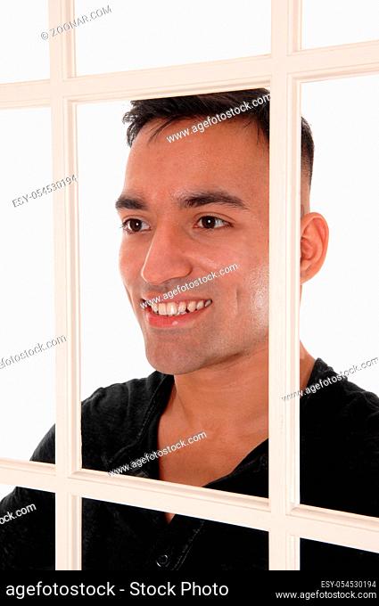 A happy east Indian man standing behind a white window frame in a black dress shirt with a big smile, isolated for white background