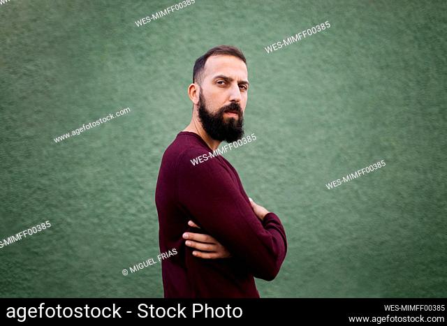 Bearded mid adult man with arms crossed standing by green wall