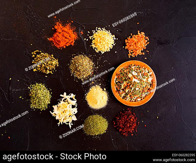 Delicious collection of ten spices for seasoning the food. Piles of grated dry vegetables and greens on dark grey surface. Top view