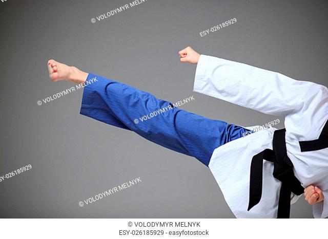 The hand and foot of karate girl in white kimono and black belt training karate over gray background