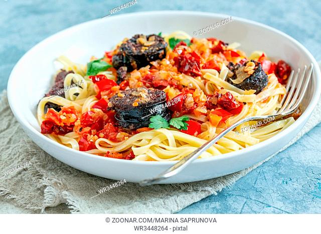 White plate with pasta, meat sauce with tomatoes, red pepper and homemade blood sausages on textured grey table, selective focus